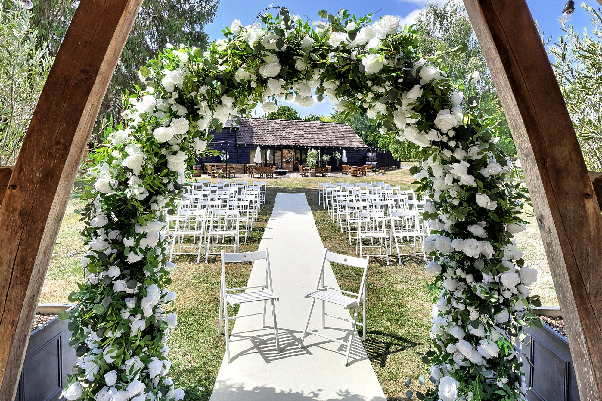 Wedding ceremony aisle framed by a white floral arch, leading to open barn doors