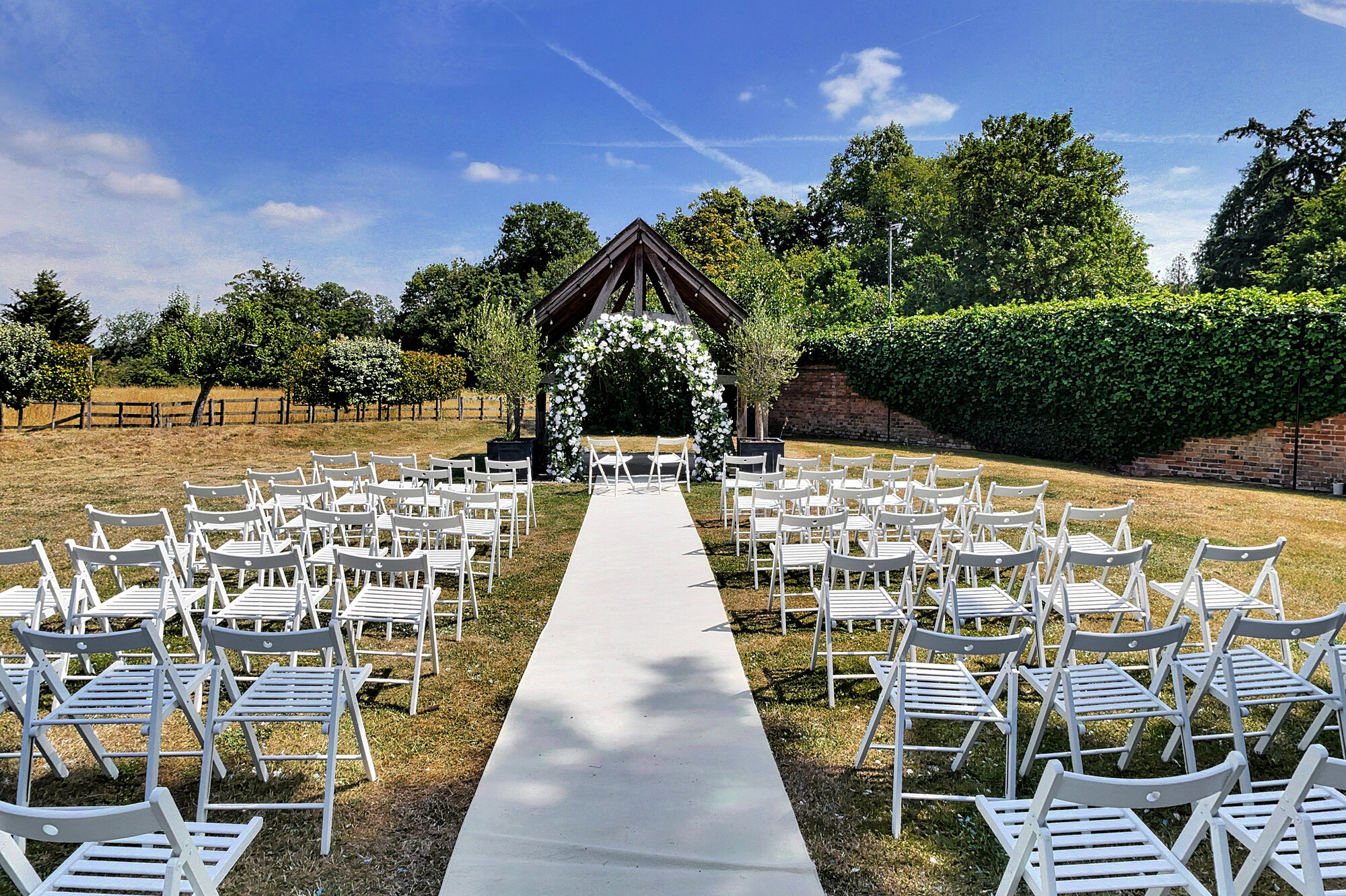 Rows of white chairs and a floral arch set out for an outdoor wedding ceremony on a lawn