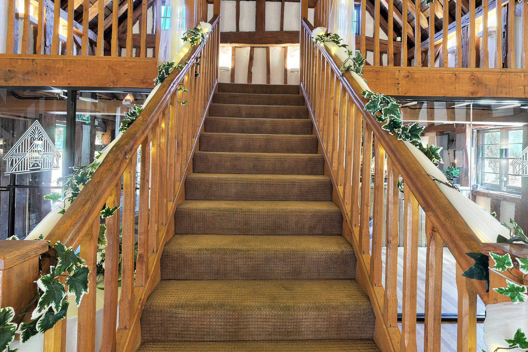 An oak staircase rising to the mezzanine, dressed with foliage garlands and fairy lights