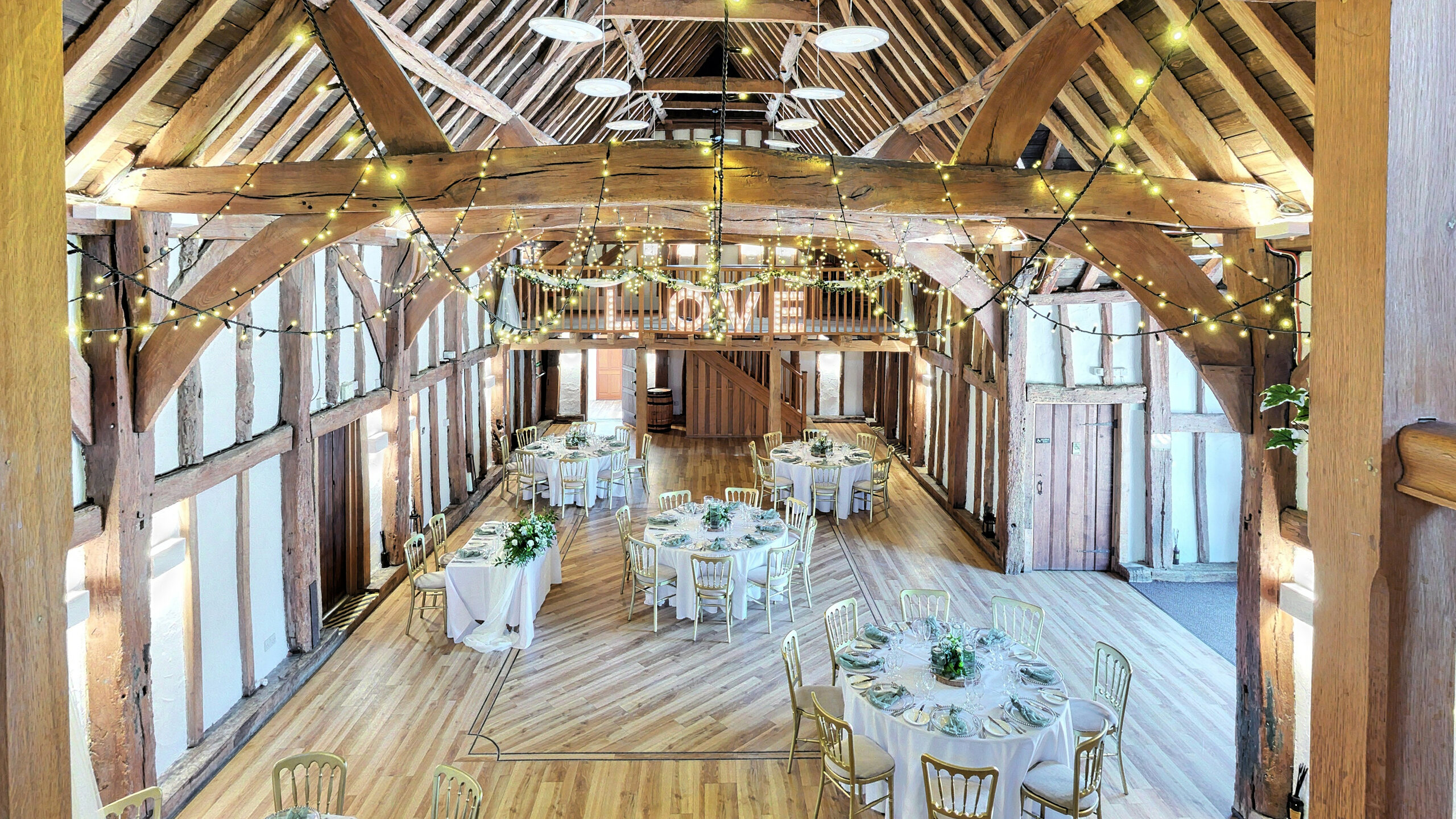 The Main Hall, viewed from the mezzanine gallery, with original oak roof trusses and fairy lights above the dressed tables