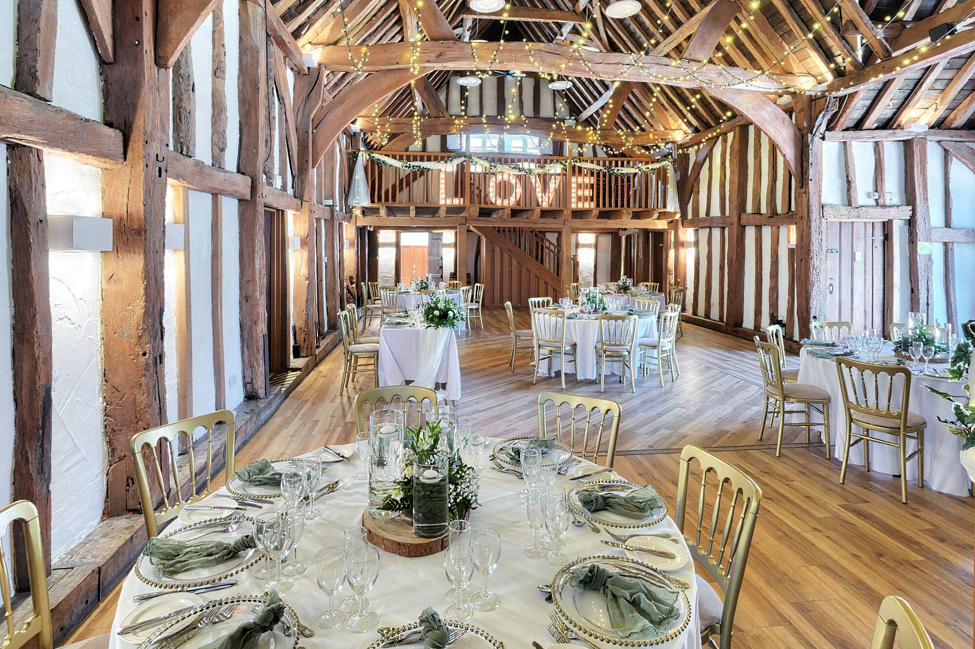 The Main Hall, a timber-framed barn dressed with round tables, florals and a LOVE light sign